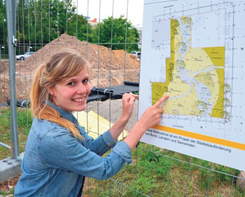 Noch ist der künftige Park fest in den Händen der Bauarbeiter. Isabell Schultz zeigt auf der Bautafel, in welchem Parkbereich später gegärtnert wird. Foto: Tanja Tröger