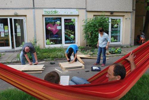 Vorbereitungen für das Projekt „Hängende Gärten“ im Mosaik. Dabei sollen die Holzpaletten als Gerüst für Blumentöpfe dienen. Sozialpädagoge Andreas Ermer (rechts in der Hängematte) ist mit einem Besucher im Gespräch vertieft. Foto: Trache