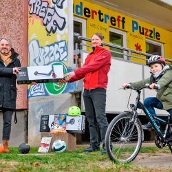 Katharina Melzer vom Kindertreff Puzzle in Gorbitz freut sich über die Spielgeräte, die ihr Kai-Michael Sigmund, Regionalleiter Dresden-West bei Vonovia, persönlich übergibt. Auch der siebenjährige Anton ist von den neuen Spiel- und Sportsachen begeistert. Fotonachweis: Vonovia SE/Frank Grätz