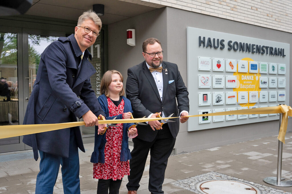 Feierliche Eröffnung nach zweieinhalb Jahren Bauzeit: Am 8. Mai haben die Initiatoren zusammen mit Unterstützerinnen und Unterstützern, Partnerinnen und Partnern sowie den künftigen Mietern die offizielle Eröffnung von Haus Sonnenstrahl gefeiert. Beim Durchschneiden des Bandes: Prof. Uwe Platzbecker, Medizinischer Vorstand am Uniklinikum Dresden, Mila sowie Andreas Führlich, Vorsitzender des Sonnenstrahl e.V. Dresden. Foto: UKDD/Michael Kretzschmar